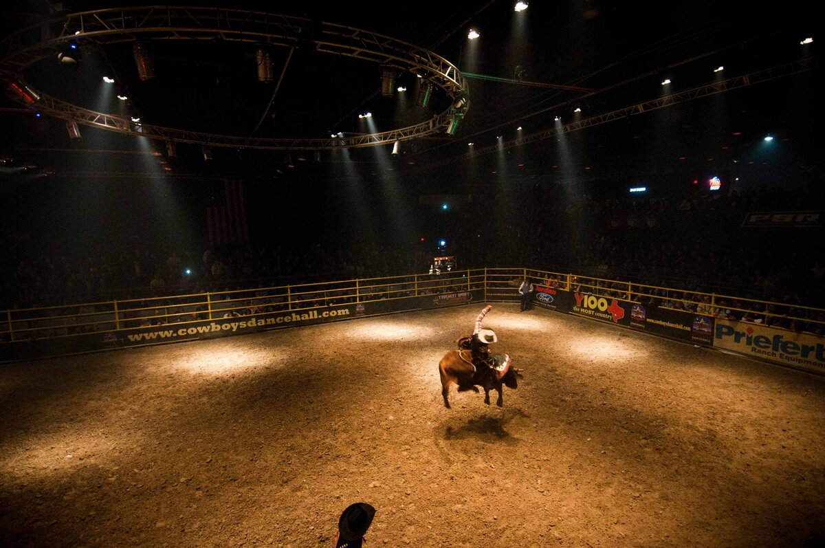 Cowboy rides bull in arena with one hand in air