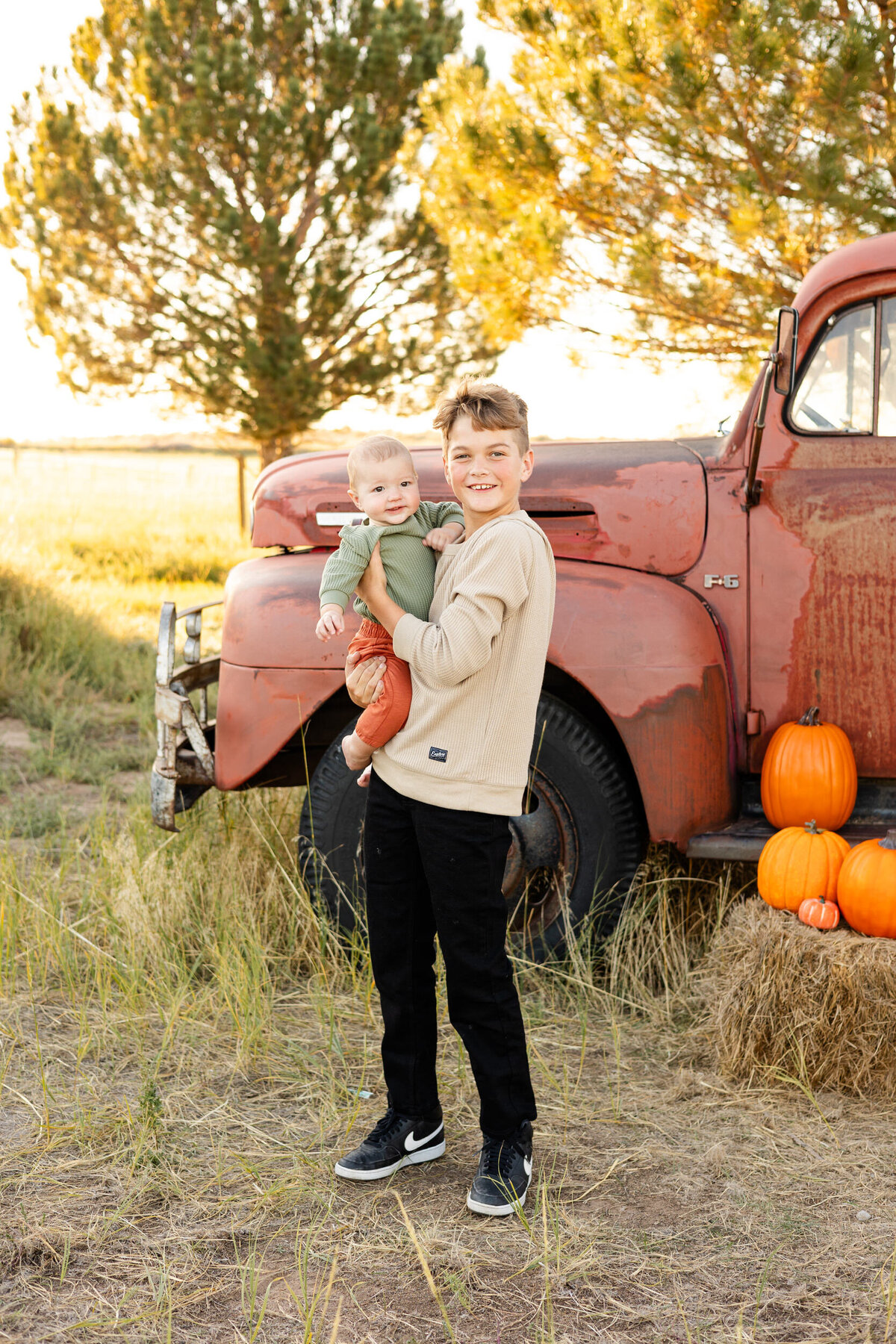 Preteen boy holds baby brother and they both smile at the camera.
