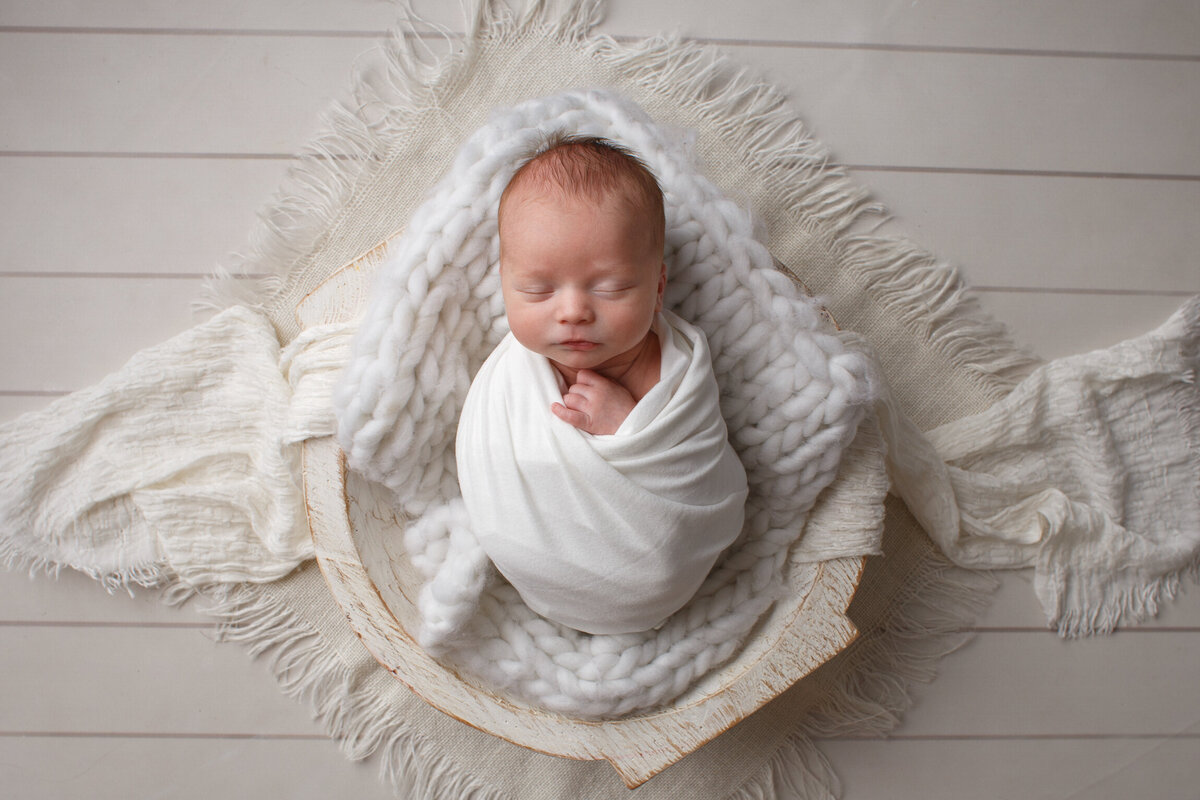 Beautiful portrait of a newborn baby in a white rap laying on a white blanket