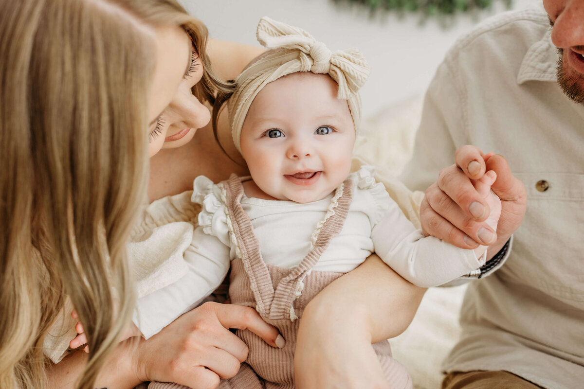 Close up image of smiling baby being held by her parents in all white studio