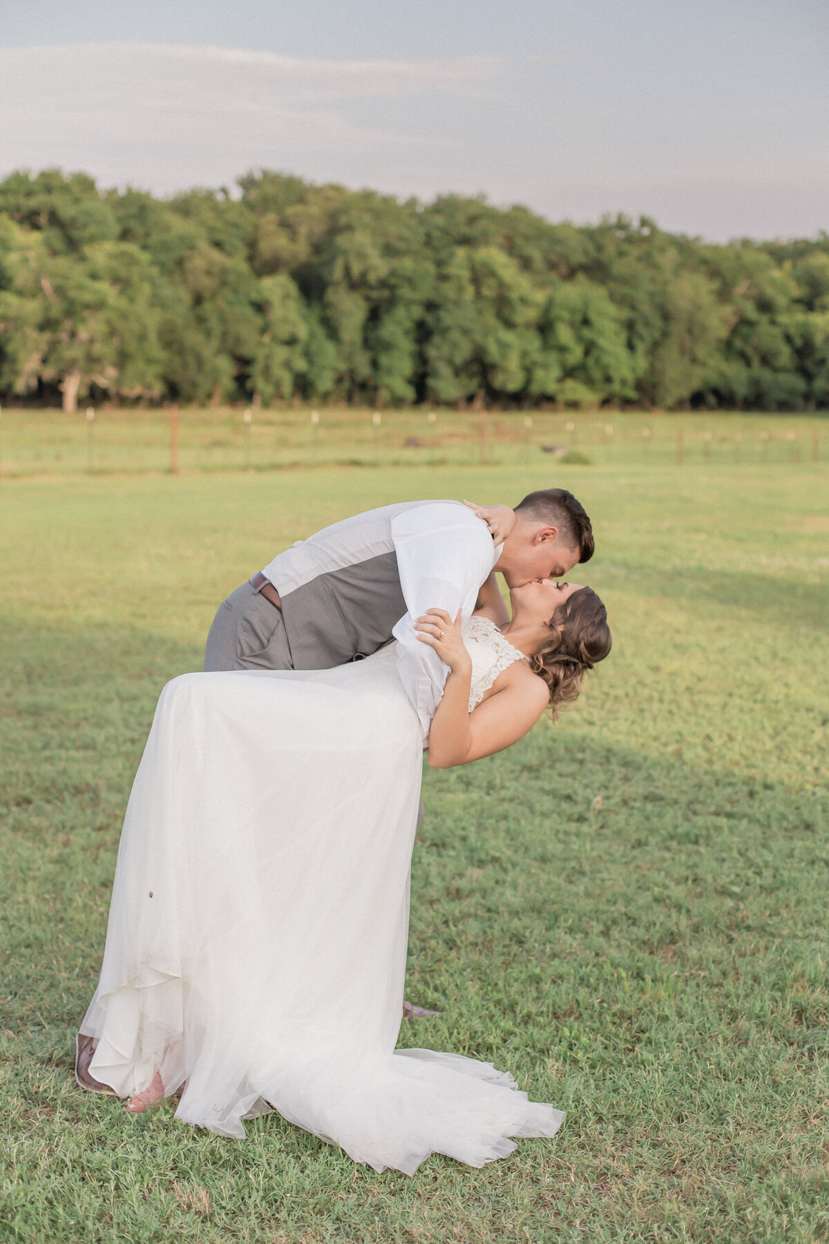 A man dips his bride and leans in for a kiss during their golden hour bridal portraits