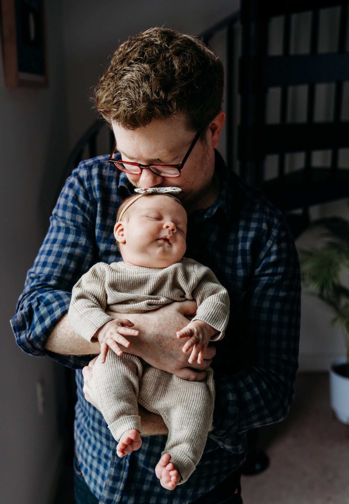 Newborn Photographer, a dad holds his baby dsughter and gives her a kiss in the living room