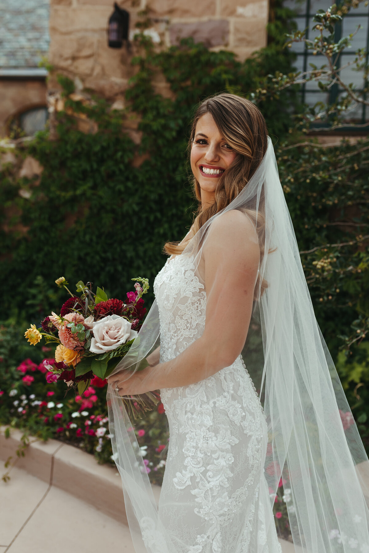 Bride poses with a red, blush, and yellow wedding bouquet.
