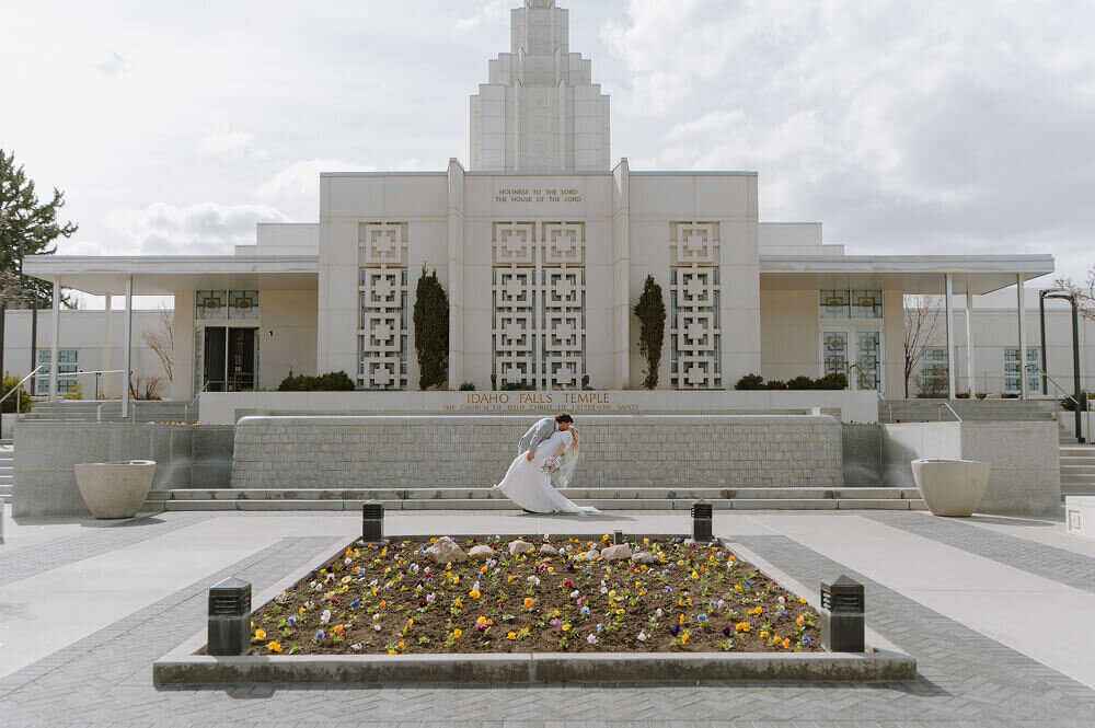 A groom dips and kisses his bride in front of an LDS temple on their wedding day near Boise, ID.