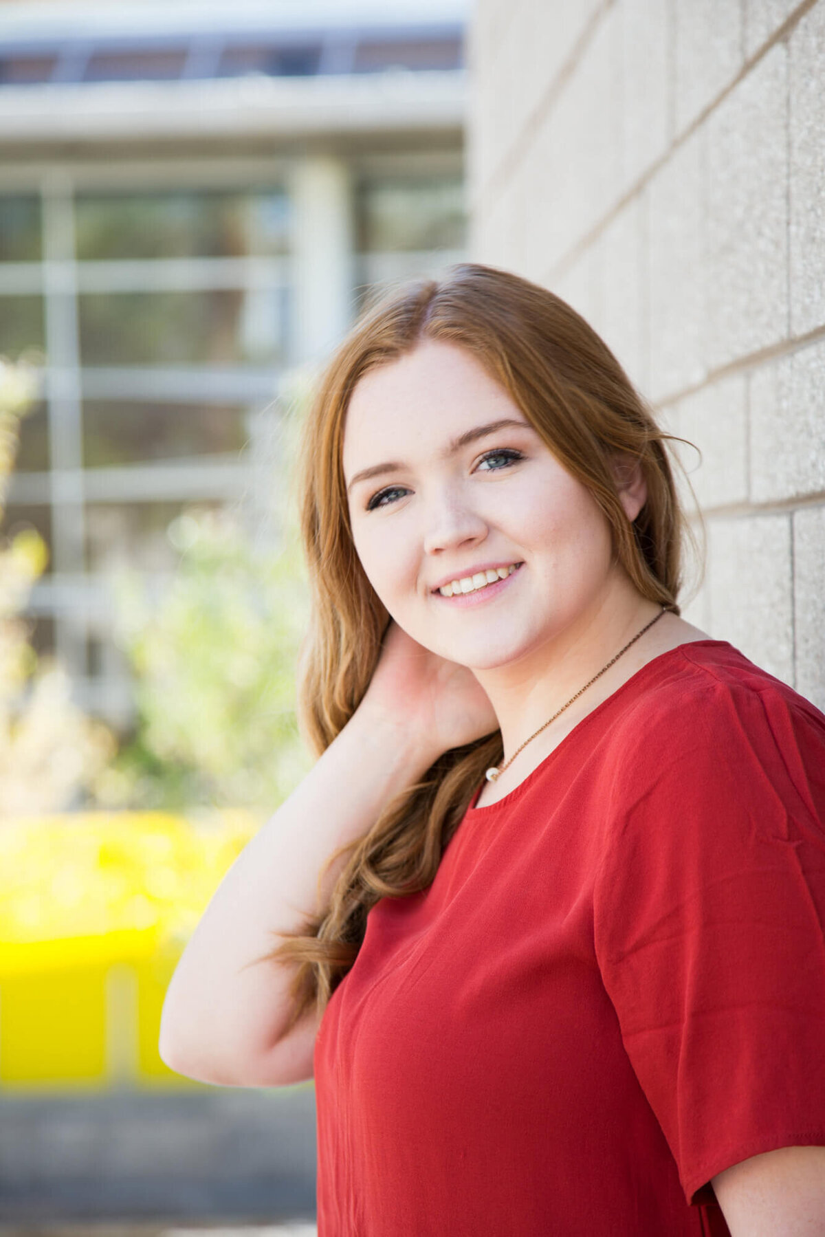 young woman smiling softly against a brick wall