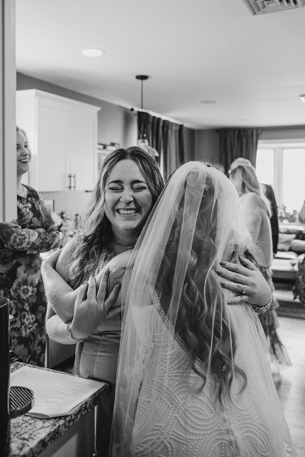 A person hugging someone in a wedding dress as they smile 