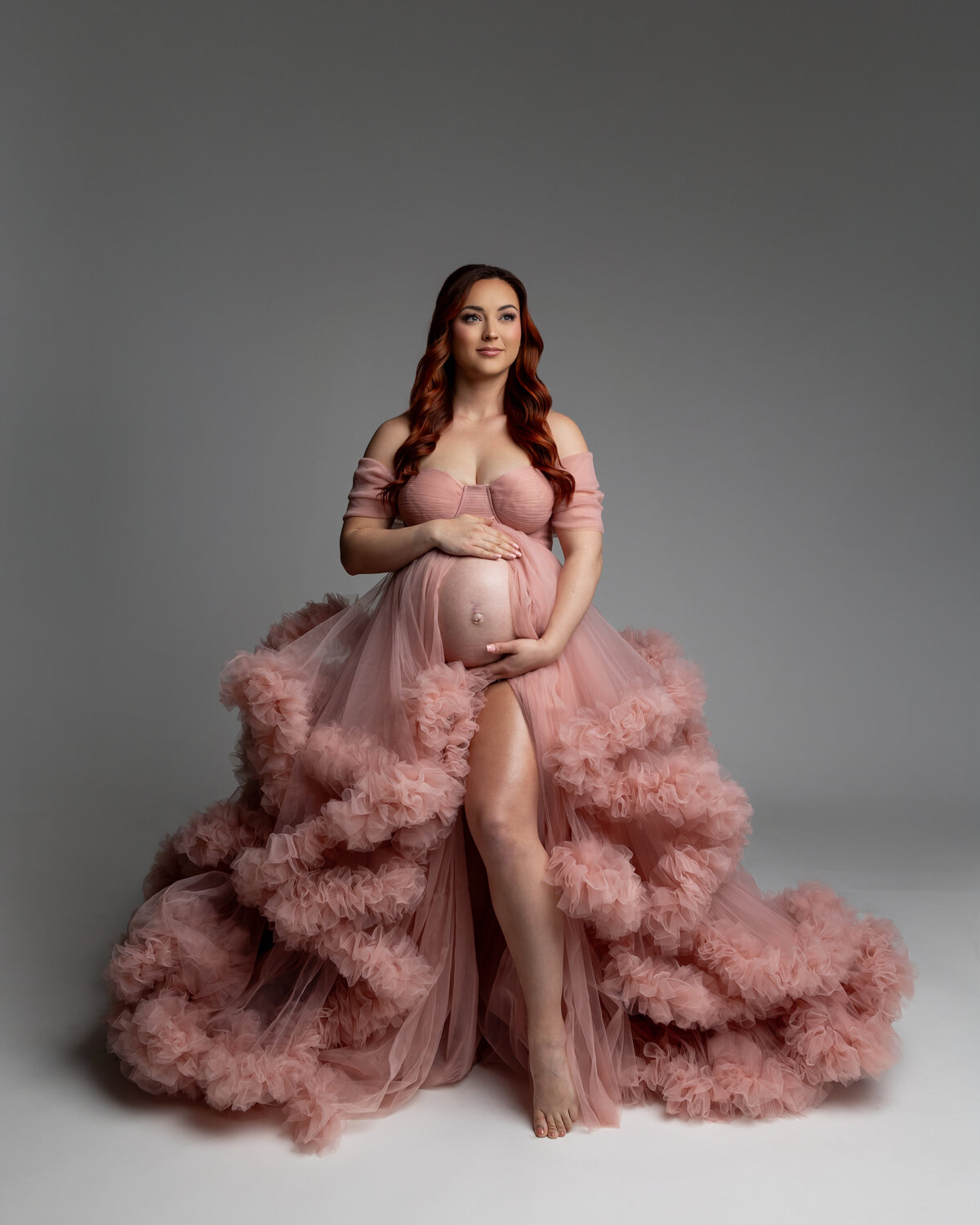 Wearing a soft pink dress, she gently holds her belly with a peaceful expression, radiating calm and beauty. Captured by Inland Empire photographer Kaitlyn Dawn Photography.