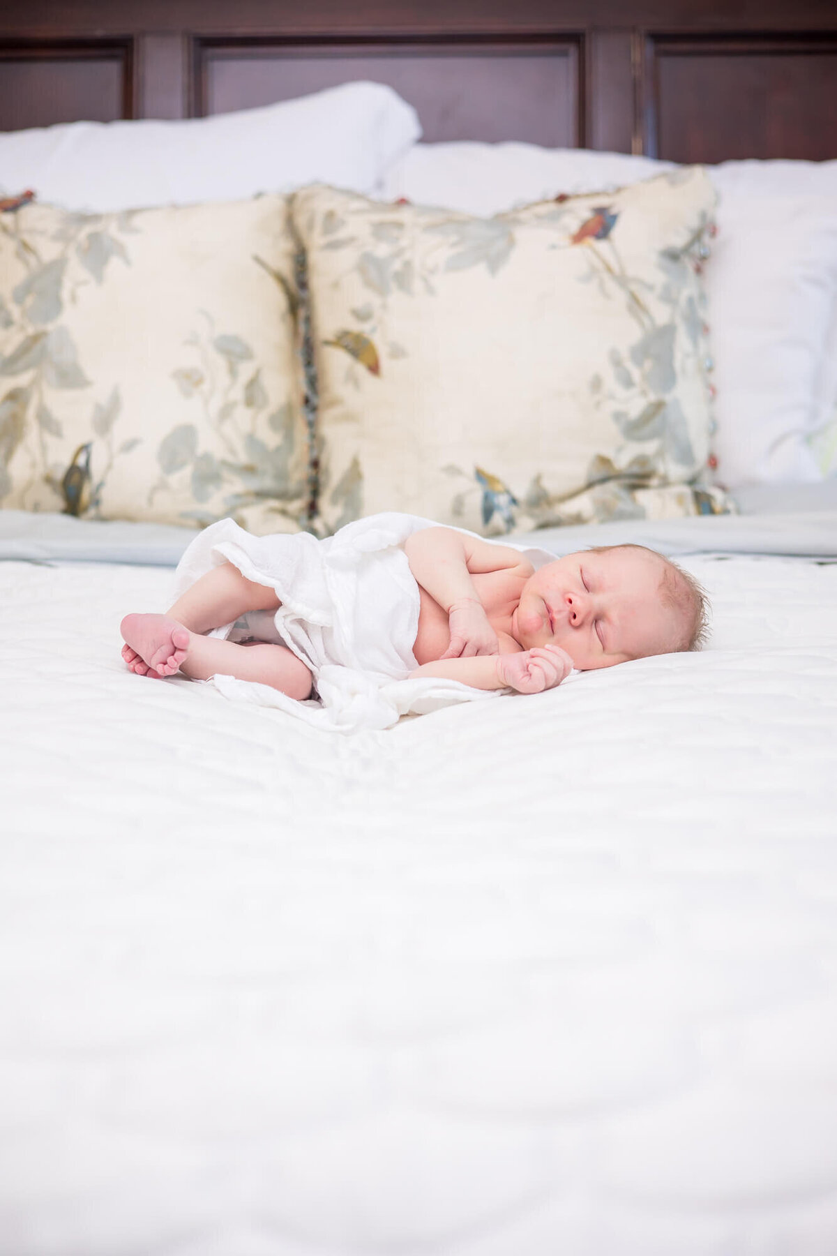 Newborn baby boy asleep on a white bed with a white swaddle over him