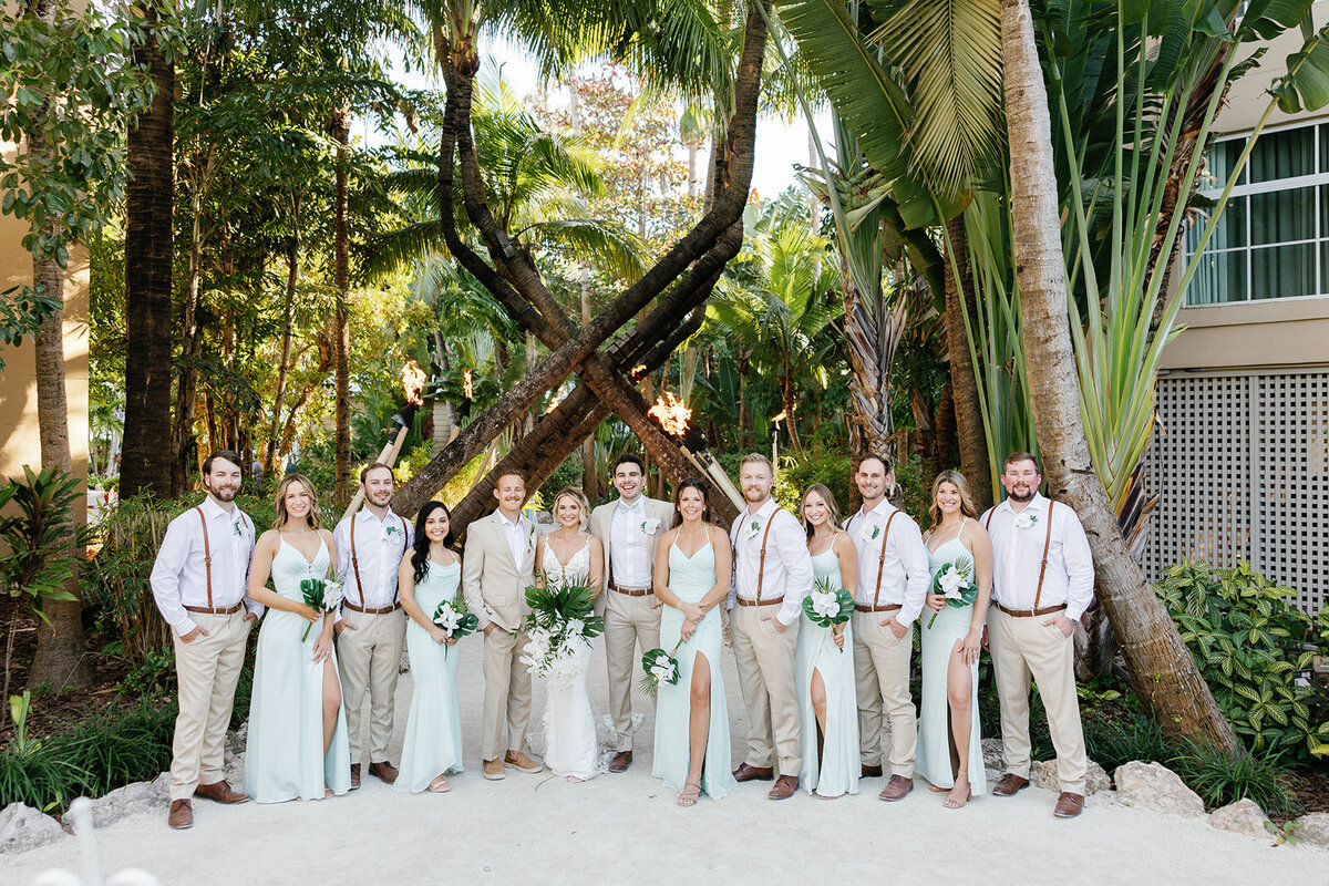  Ashley, Hunter, and their wedding party pose under lush greenery and palm trees.