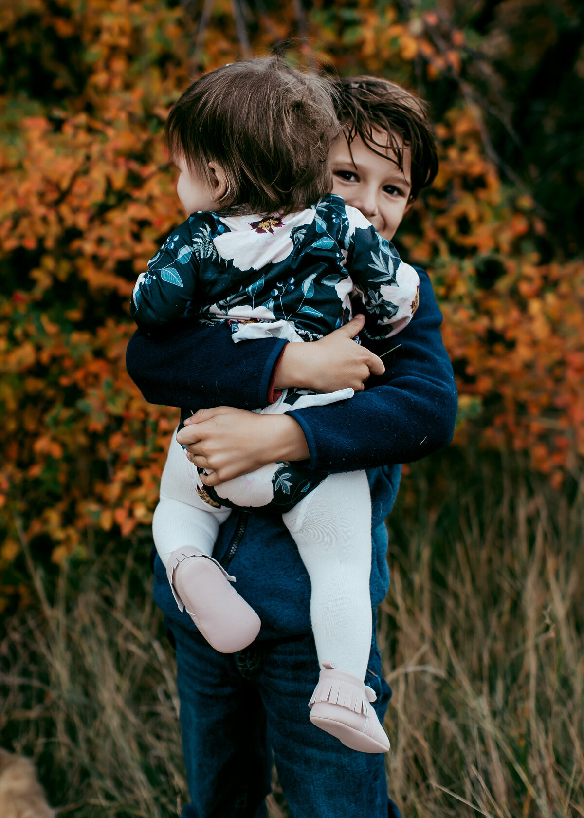 big brother carries baby sister during fall family photos in Boulder colorado