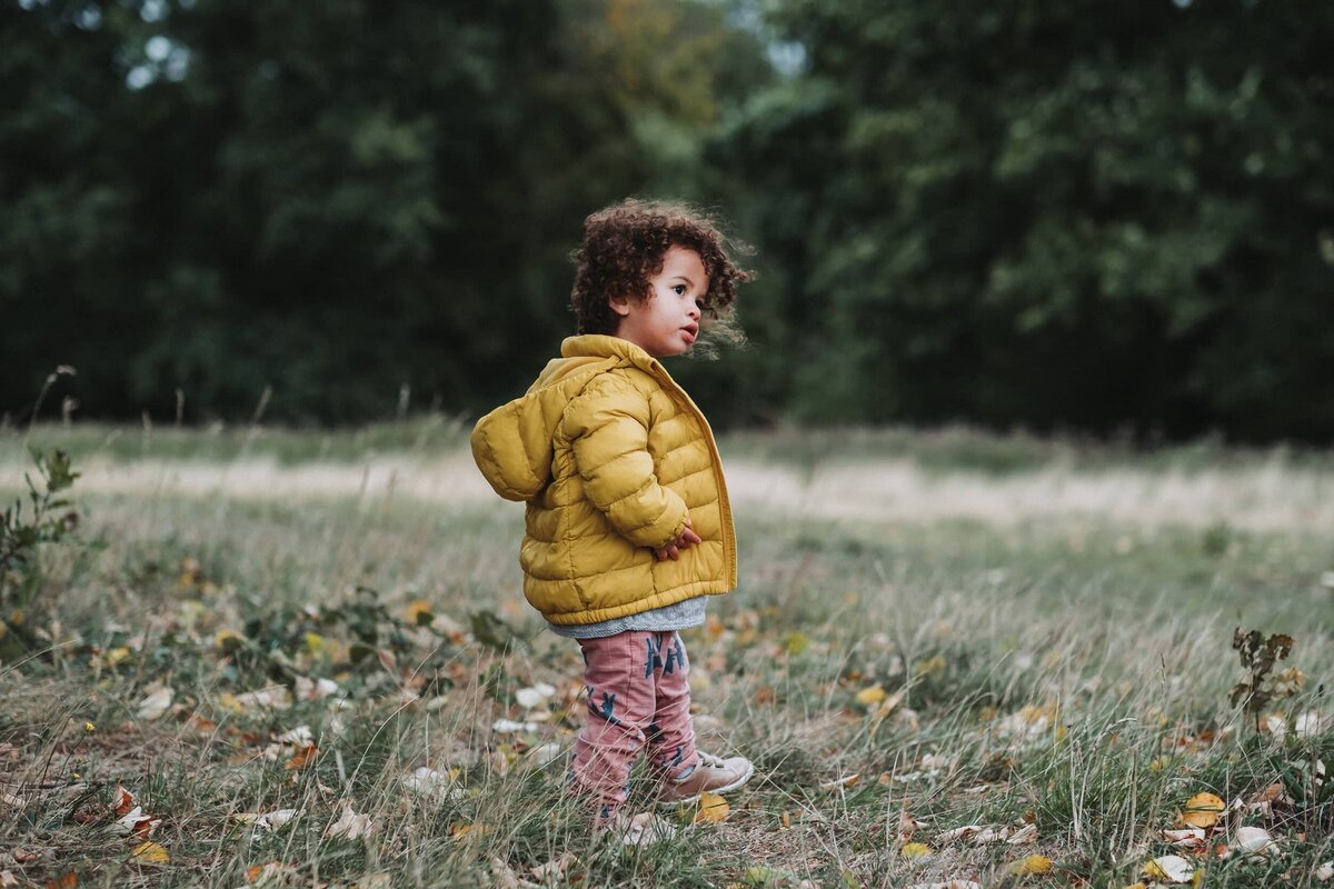 Girl in yellow puffy coat walks in the grass in Hampstead London