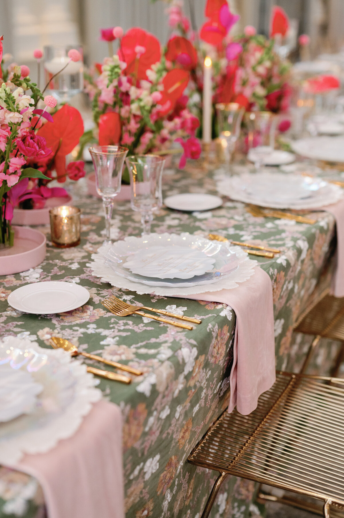 A beautifully designed wedding table setting with gold-accented chairs, delicate gold utensils, and frosted white dinnerware. The floral-patterned linens and soft pink centerpieces add warmth and sophistication, making this an ideal choice for couples seeking a luxury reception aesthetic.