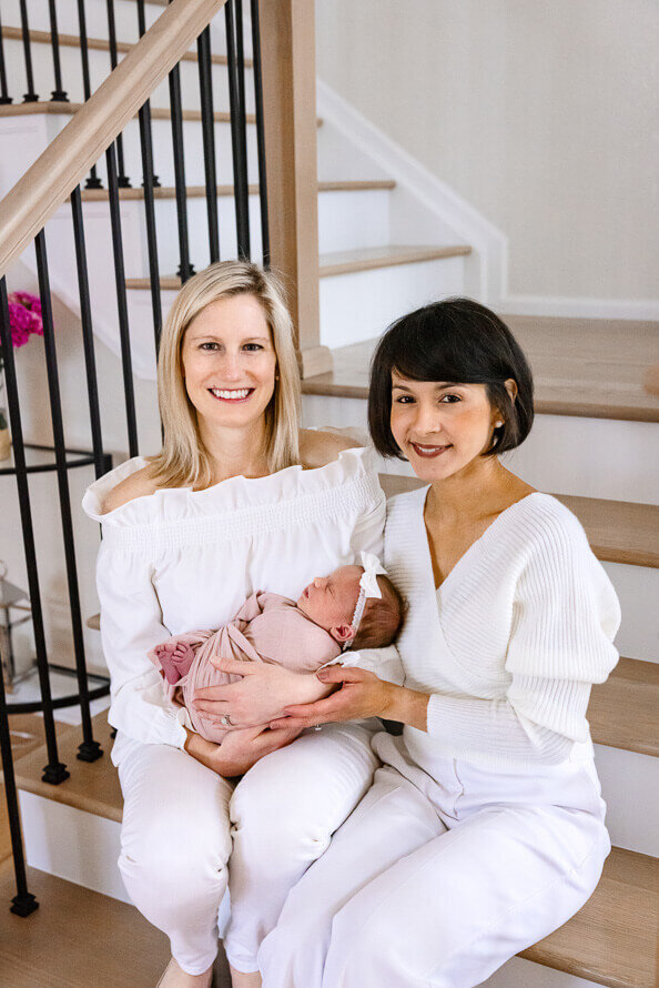 Tow moms pose and smile with their new baby girl.