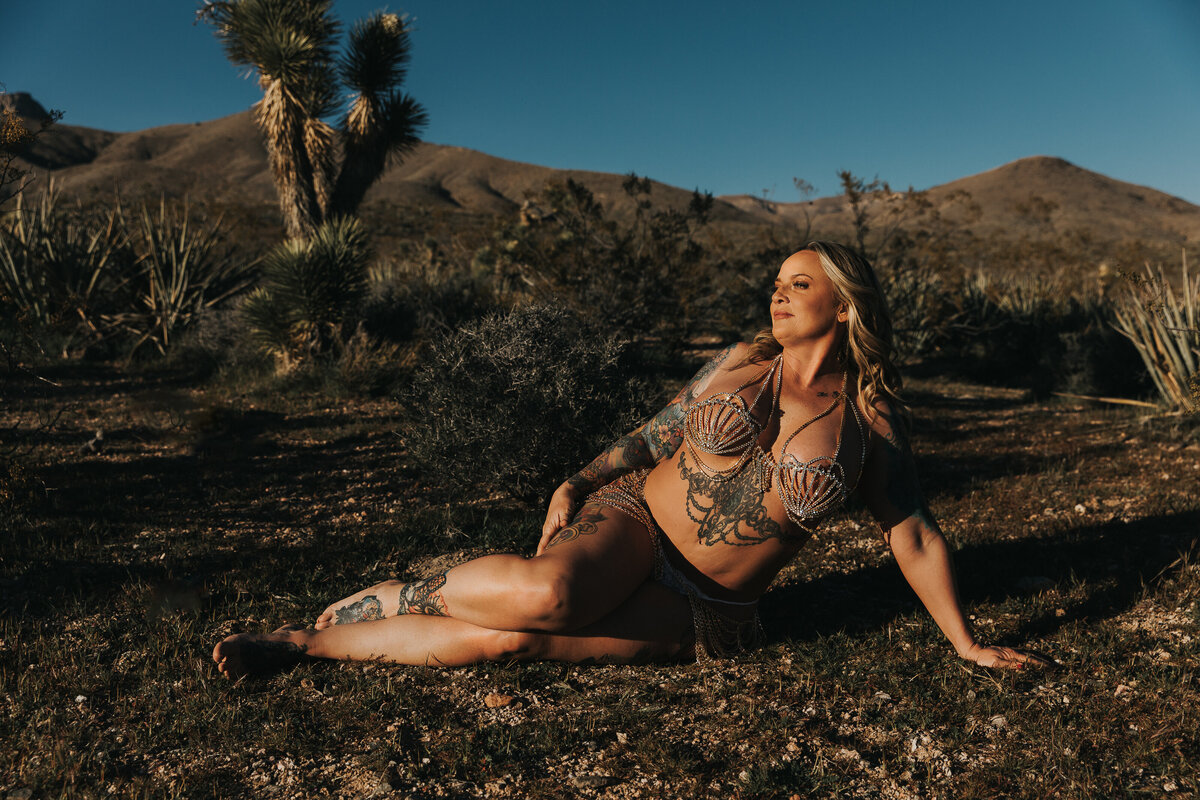 Woman perched on her side on the desert. She is wearing a beautiful crystal two piece outfit