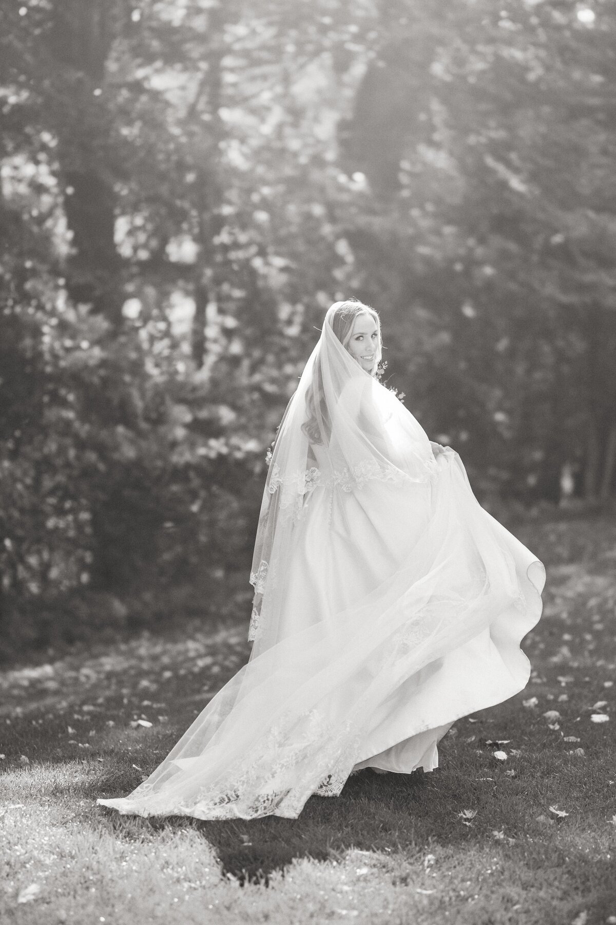 Black and white image of bride  walking under the trees in Litchfield
