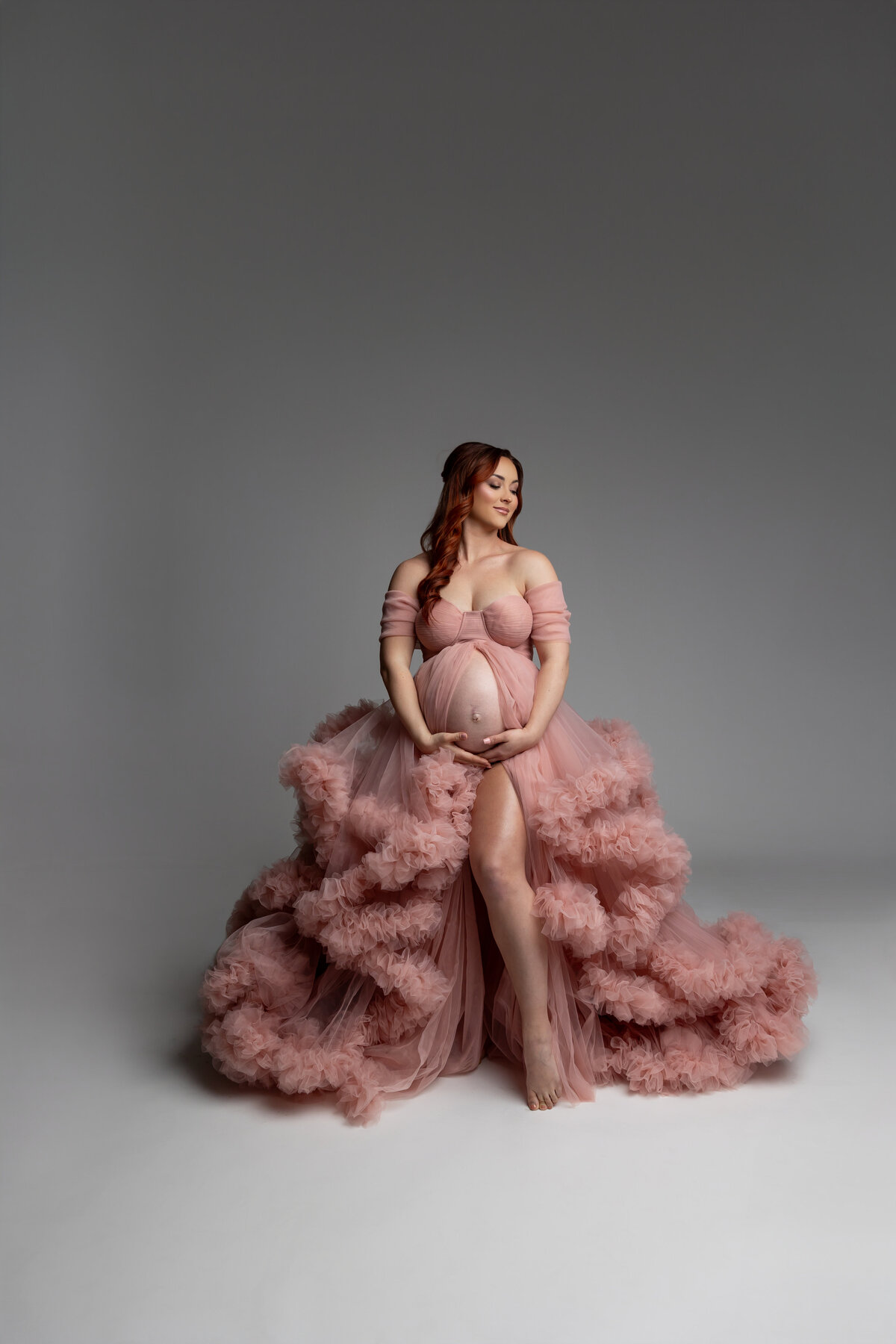 A mama-to-be in a soft pink dress, gently cradling her belly. Captured by Inland Empire maternity photographer Kaitlyn Dawn Photography during a serene, loving moment.