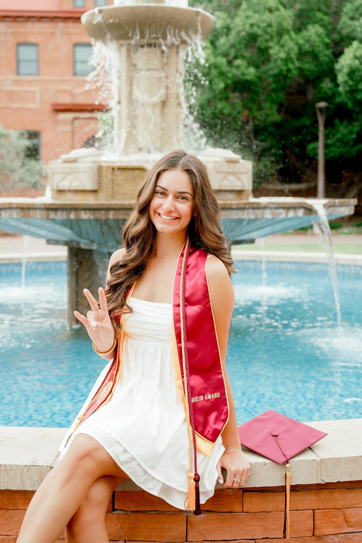 senior girl at ASU holding forks up sitting by the fountain
