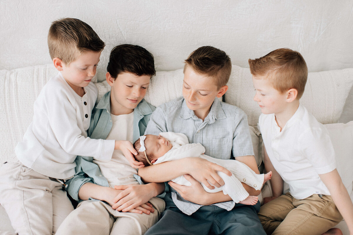 four big brothers sitting on the bed looking down at their newborn sister