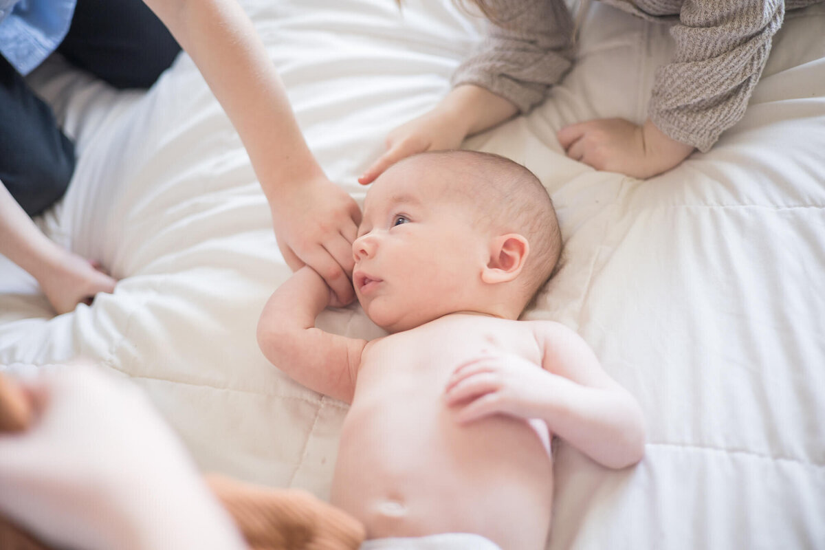 newborn baby boy laying on a white bed wirrounded by adoring young siblings