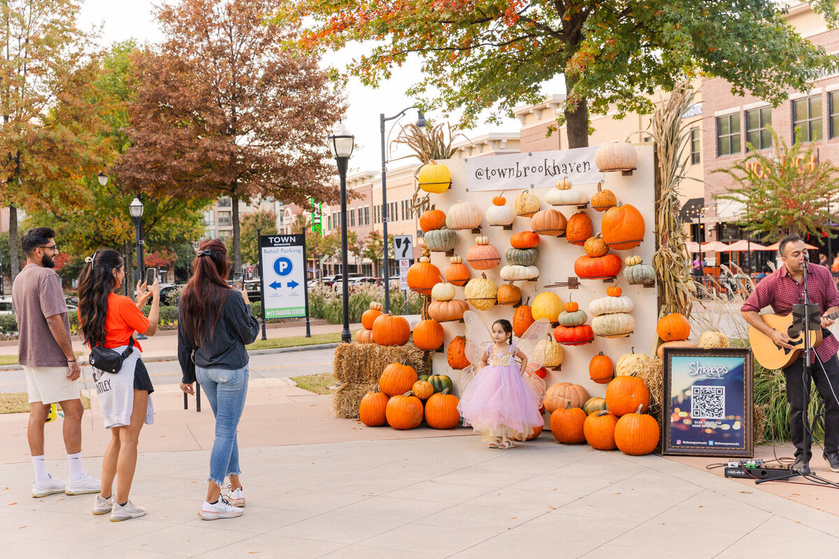 Pzrents taking pictures of their daughter standing in front a a wall of pumpkins during Atlanta Brookhaven Town fall festival  event photographer| Laure Photography