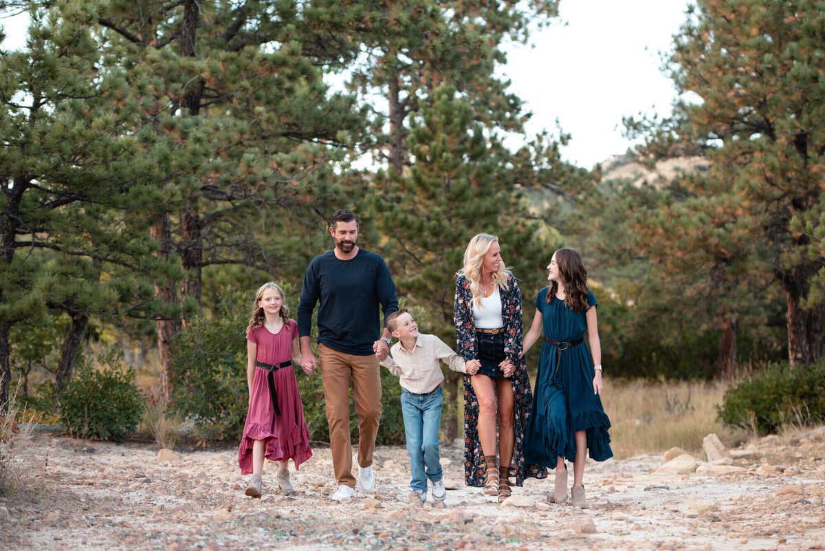 An image from a Denver family photographer of a family of 5 playing and laughing while holding hands and walking up a trail