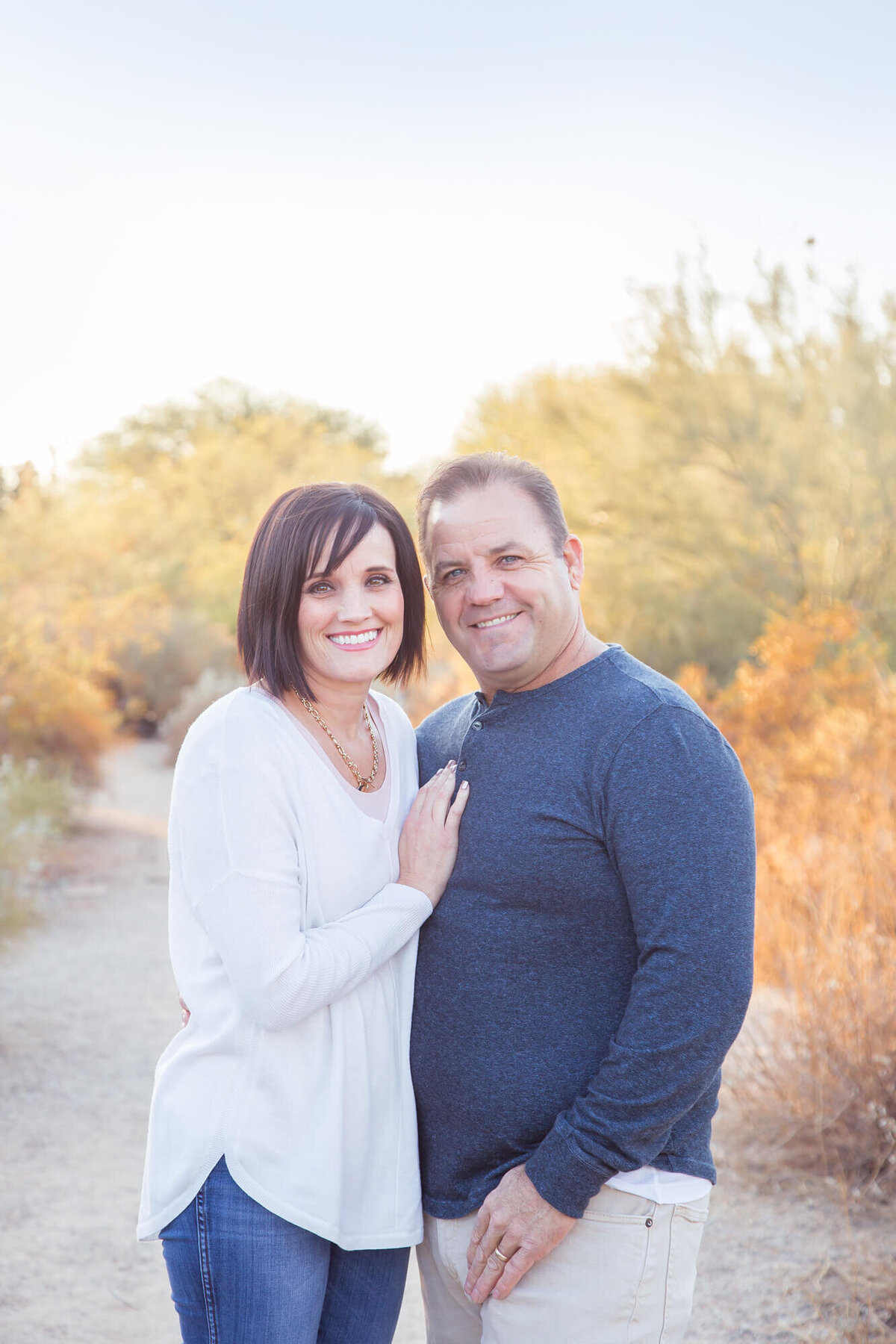 brown haired couple smiling on a desert path wearing blue and white