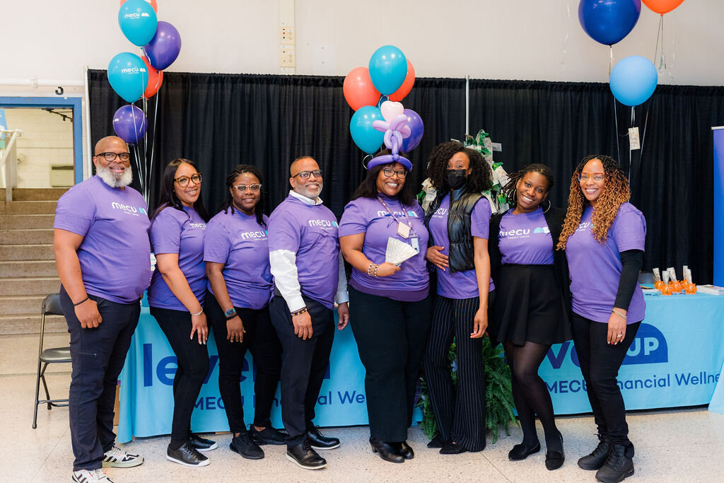 A group of people in purple shirts pose in front of a blue table.