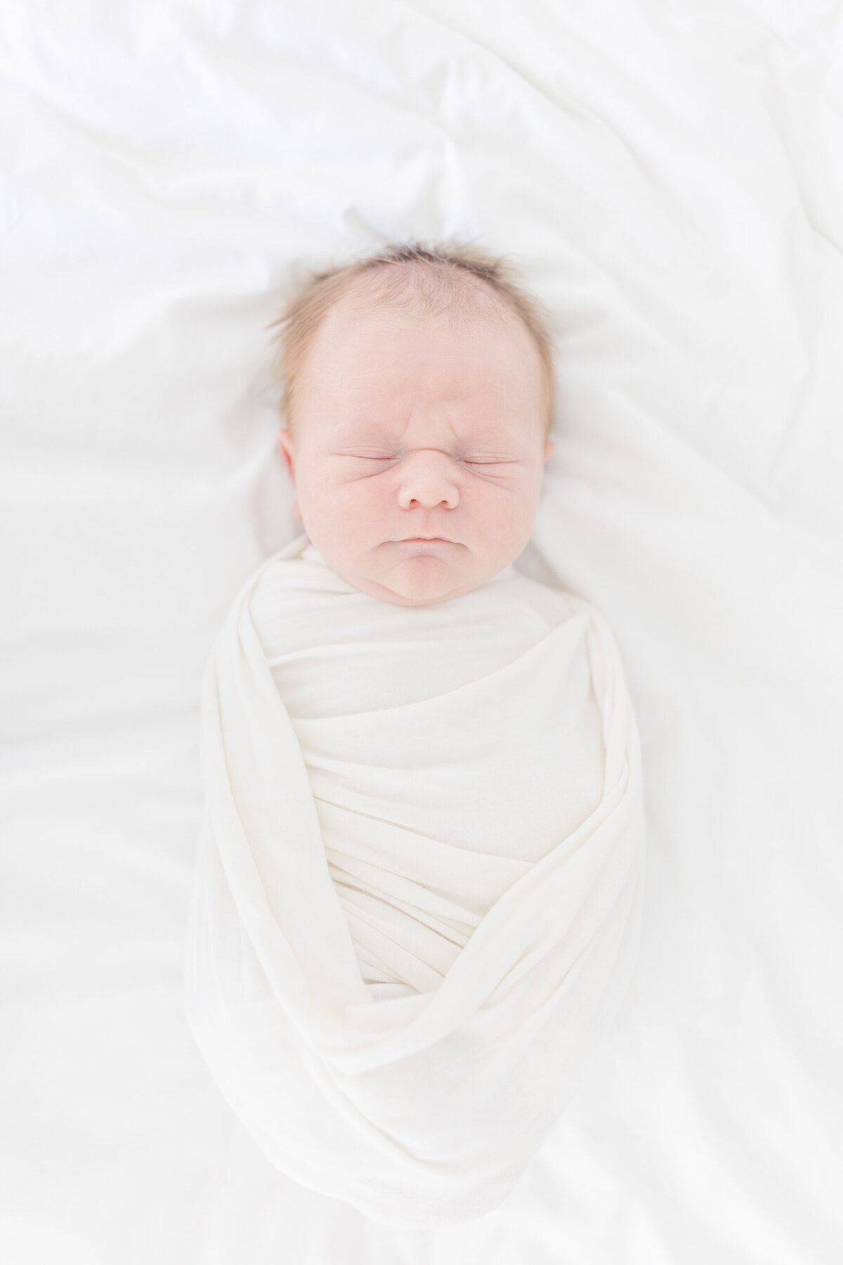 A timeless heirloom-style newborn session featuring a bright, white aesthetic. The soft, natural light highlights the baby's delicate features as they rest peacefully, capturing every tiny detail with warmth and elegance. This classic portrait showcases the baby’s face in a pure and airy setting, creating a cherished keepsake for generations to come.
