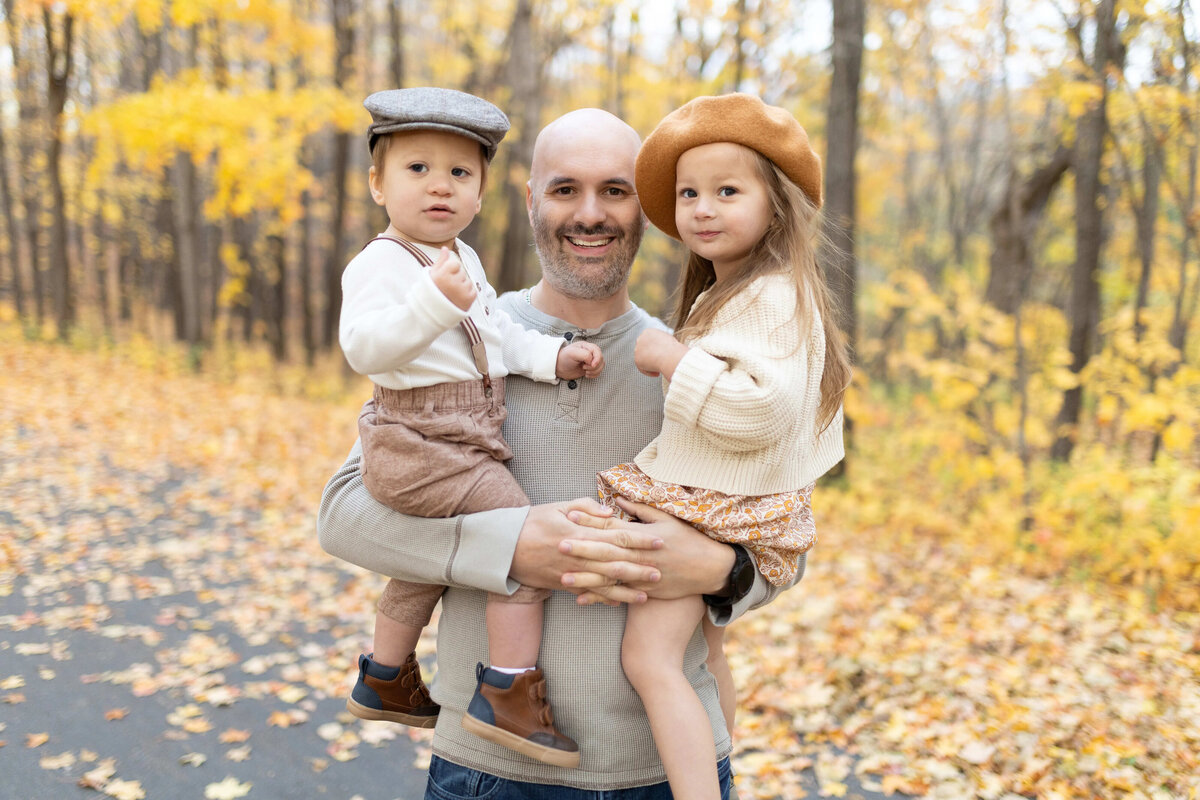 Dad holding two toddlers on autumn trail - fall family photo session in Maple Grove