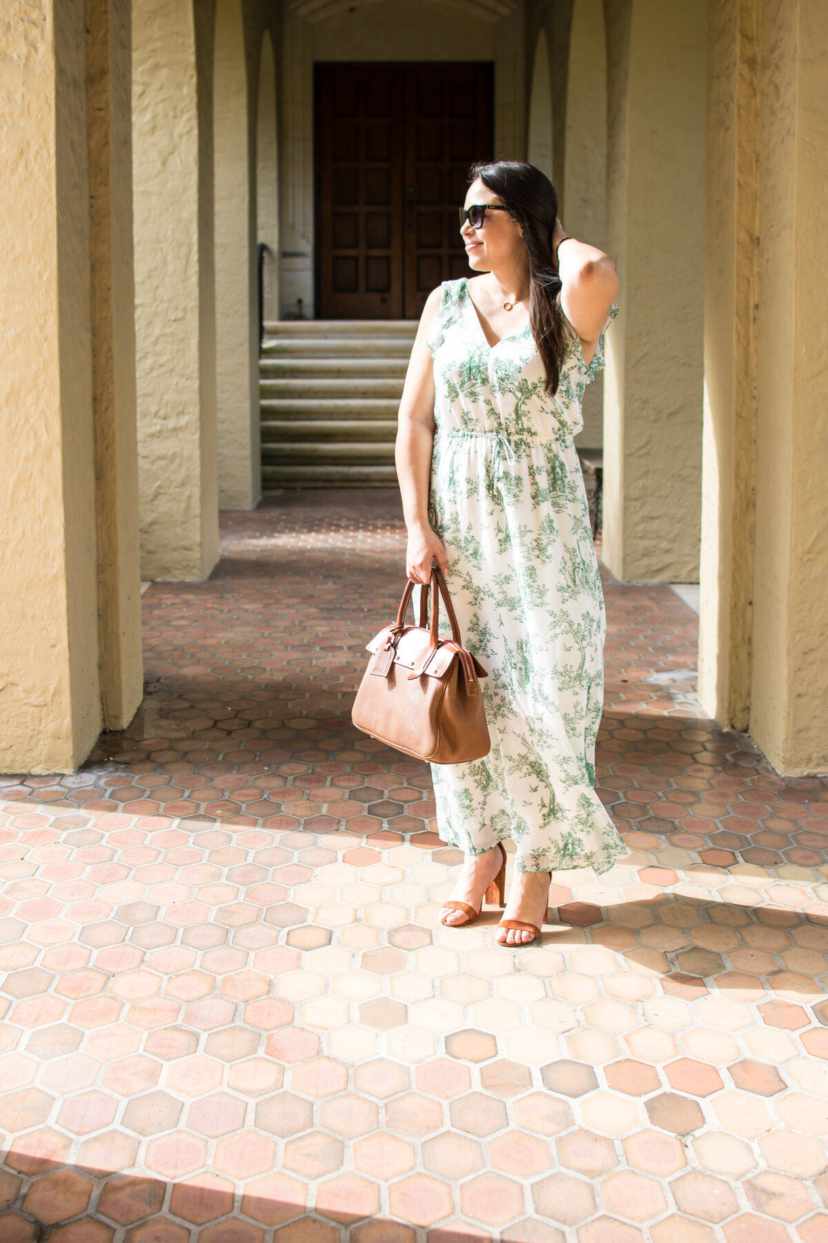 Woman in green and white dress touches her hair while stopped in the sunlight under a covered walkway