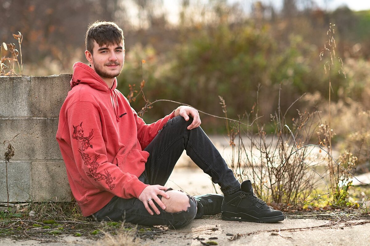 High school guy wearing red Supreme sweatshirt seated on ground