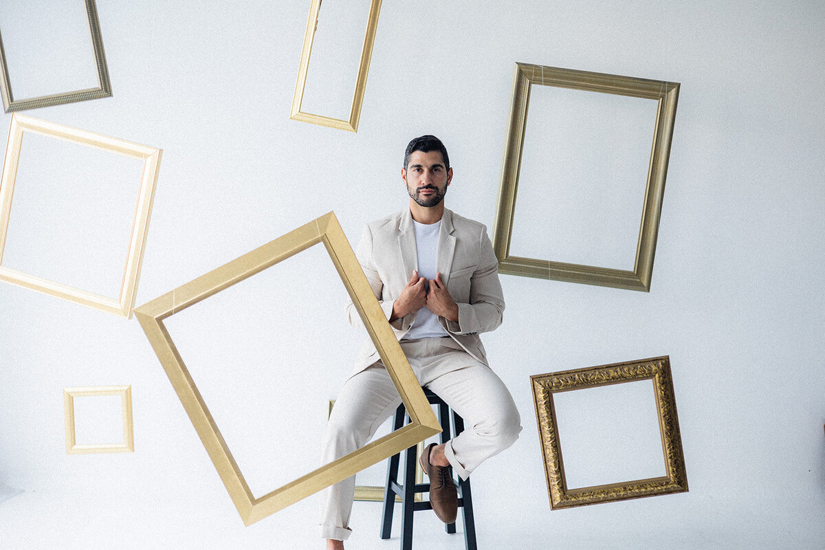 A man sits on a stool surrounded by frames