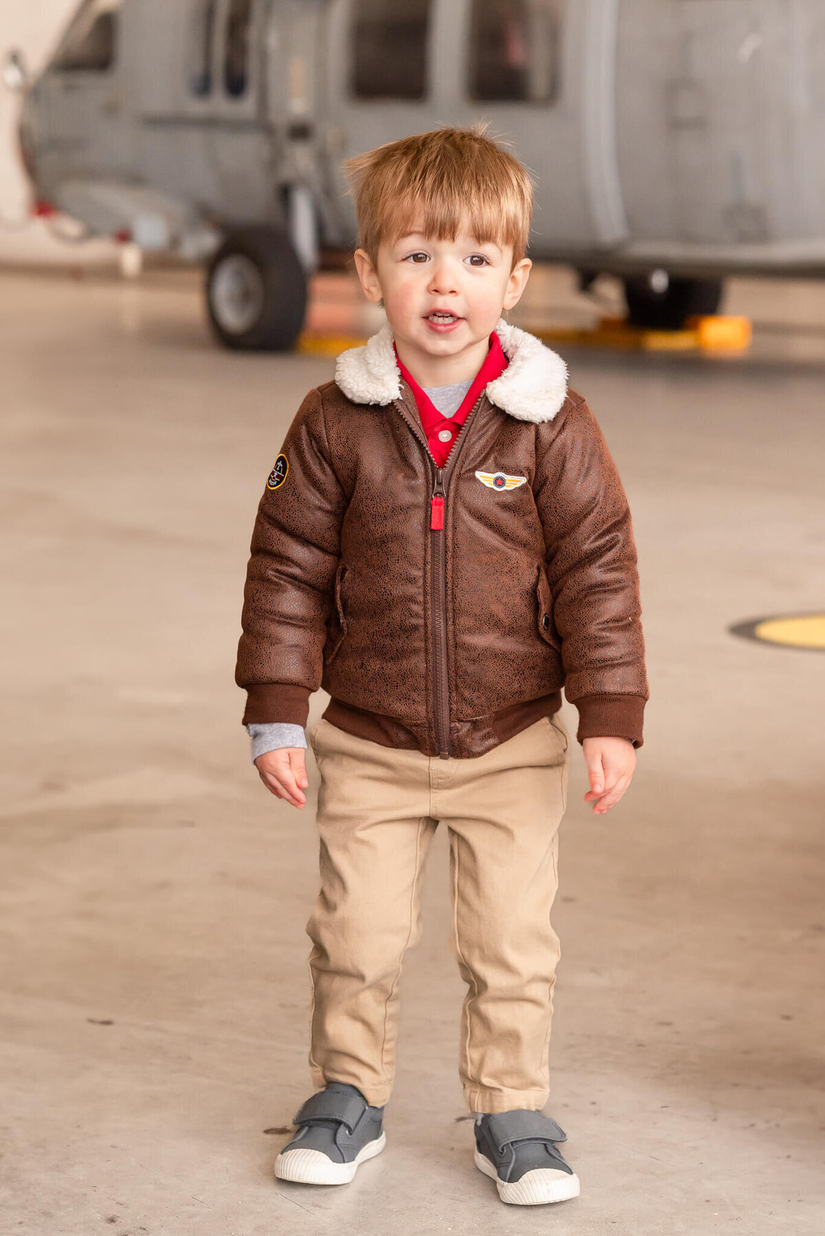 A young boy, wearing a top gun style flight jacket, waits for his dad to come home at a military homecoming.