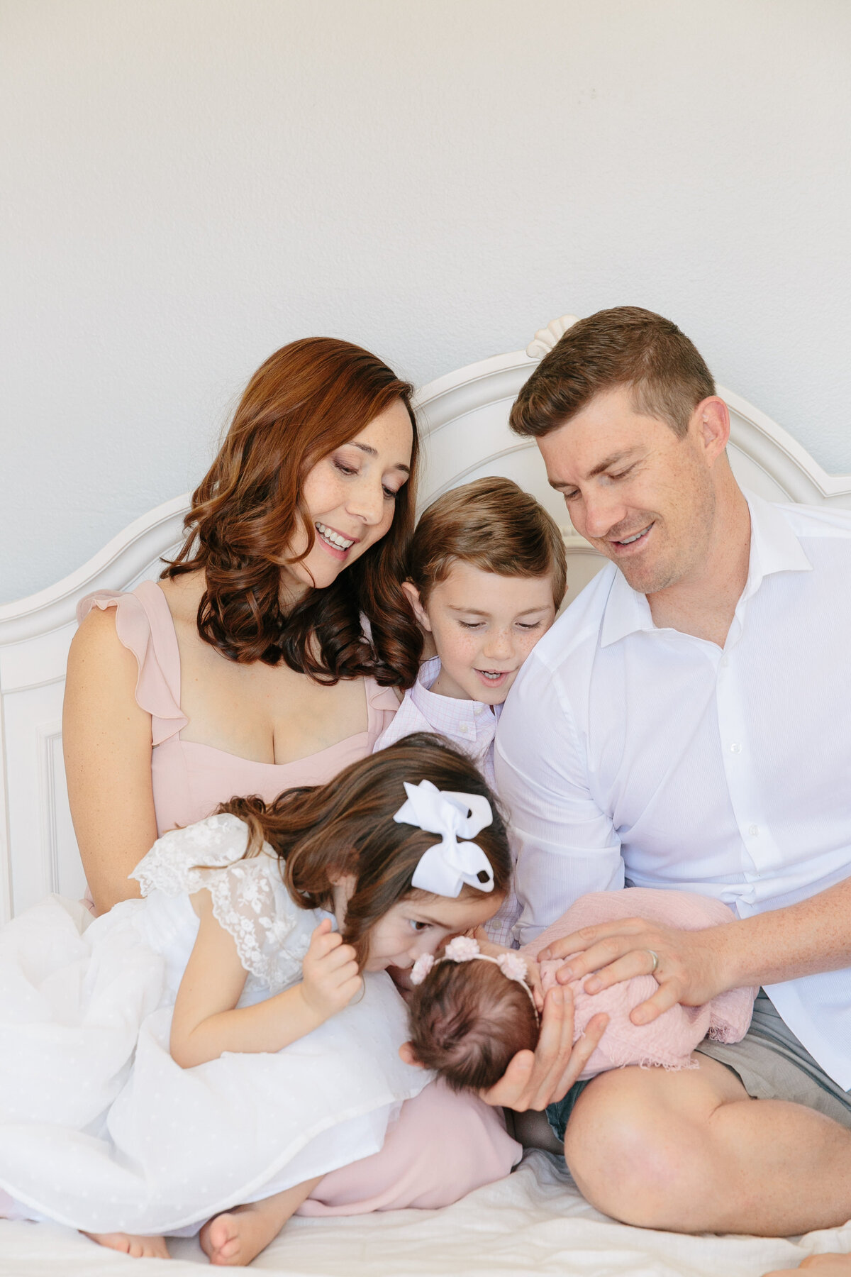 A family sitting on a bed smiling at a newborn baby