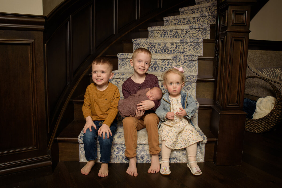 Family portrait of four children including a newborn baby sitting on the stairs of their home in Green Bay, Wisconsin.