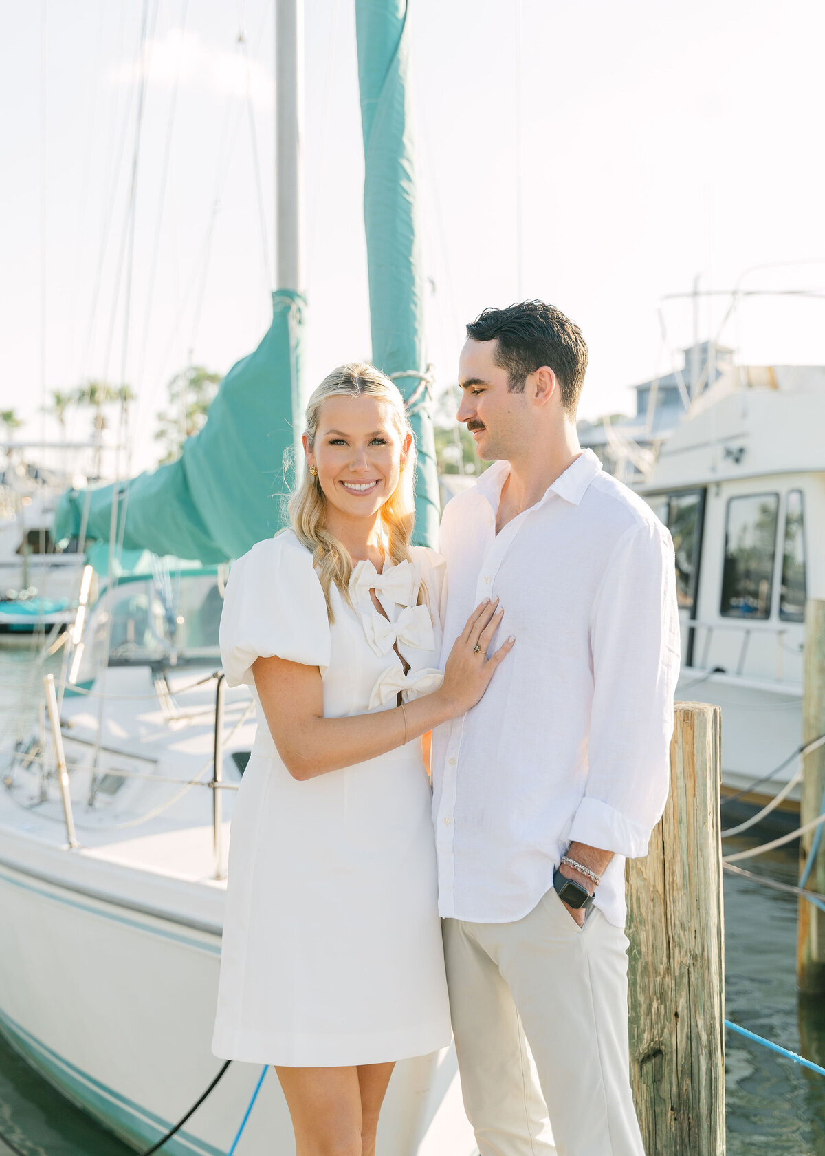 couple standing on a dock in front of a sailboat
