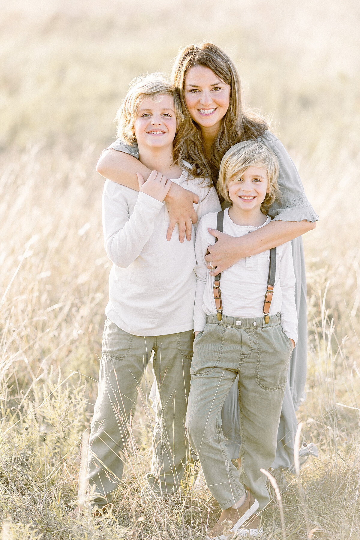 A mother posing in the middle of a Frisco area park holding her two sons tightly as they all smile and pose for their family photographer.