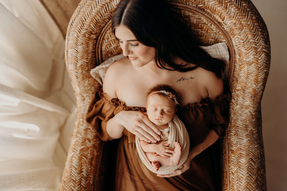 gorgeous mother holds swaddled newborn in a brown dress