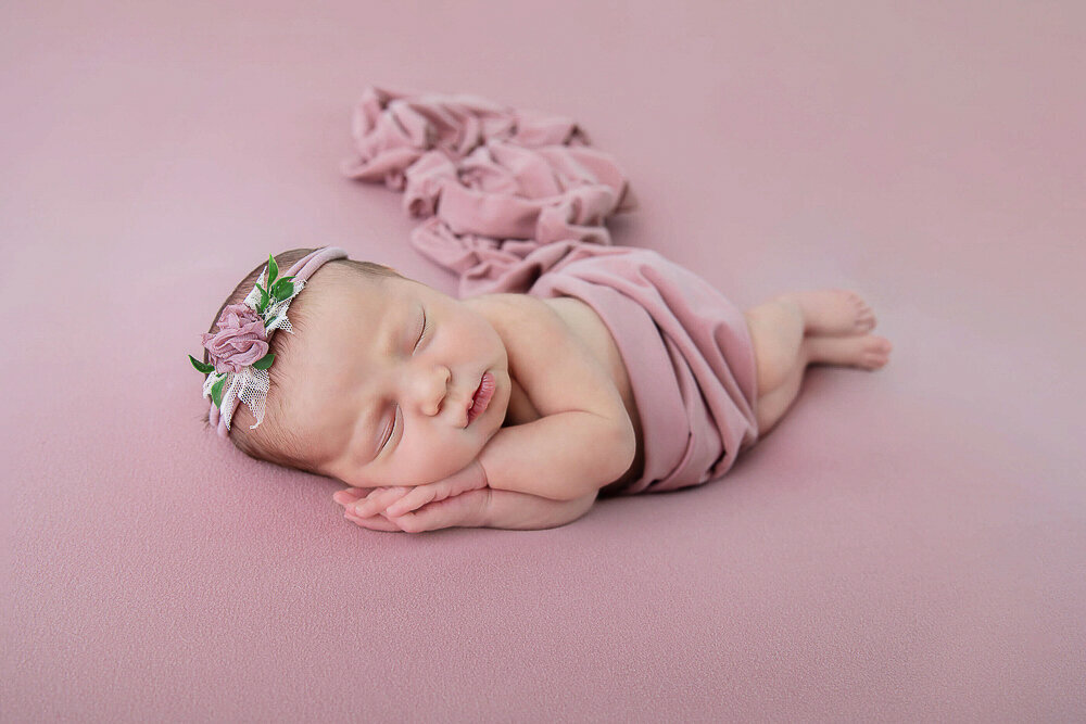 newborn baby girl wrapped in pink laying on a pink background.