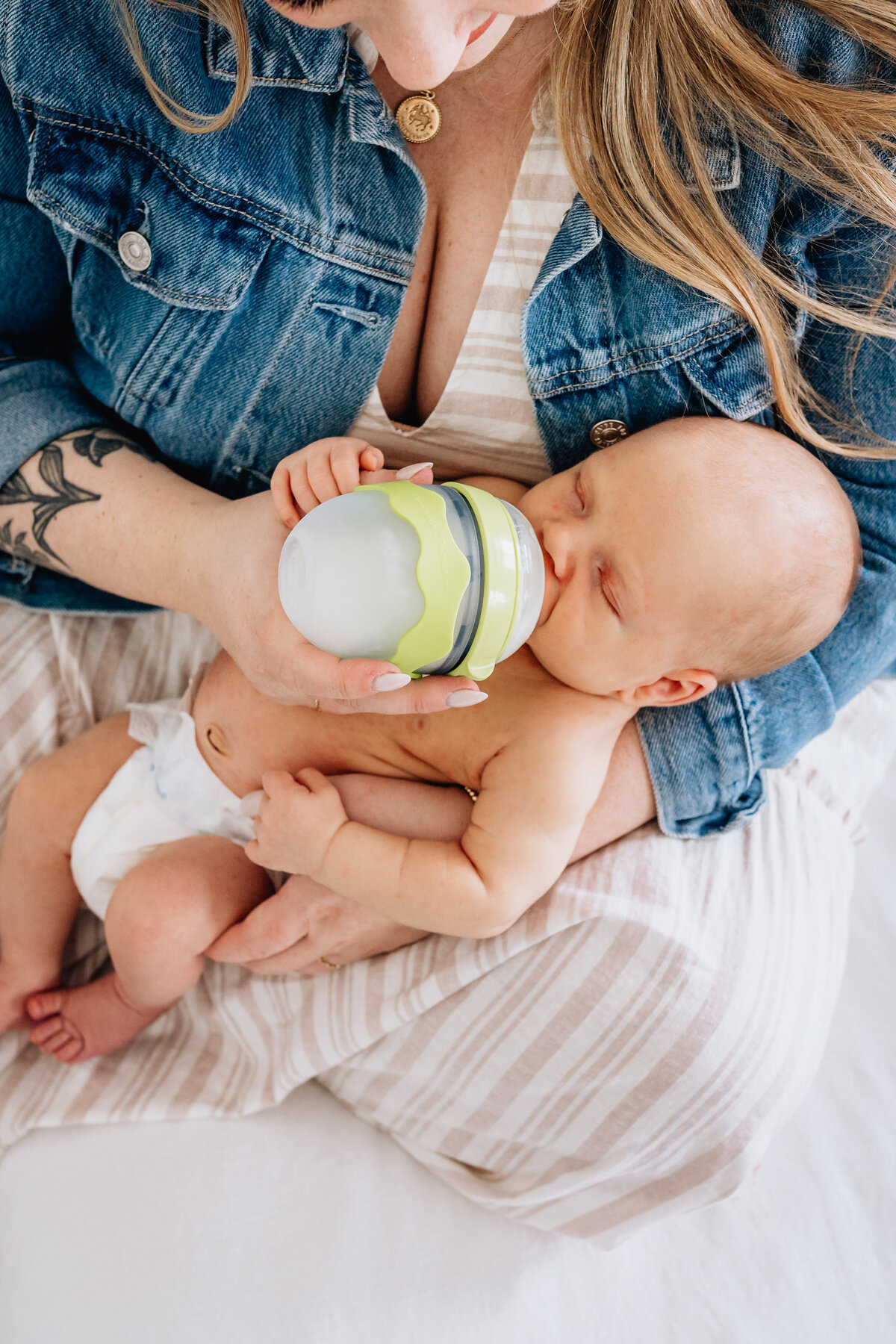 A close-up of a mother feeding her newborn baby with a bottle. The baby, dressed only in a diaper, is cradled in the mother’s arms as she tenderly holds the bottle to the baby’s mouth.