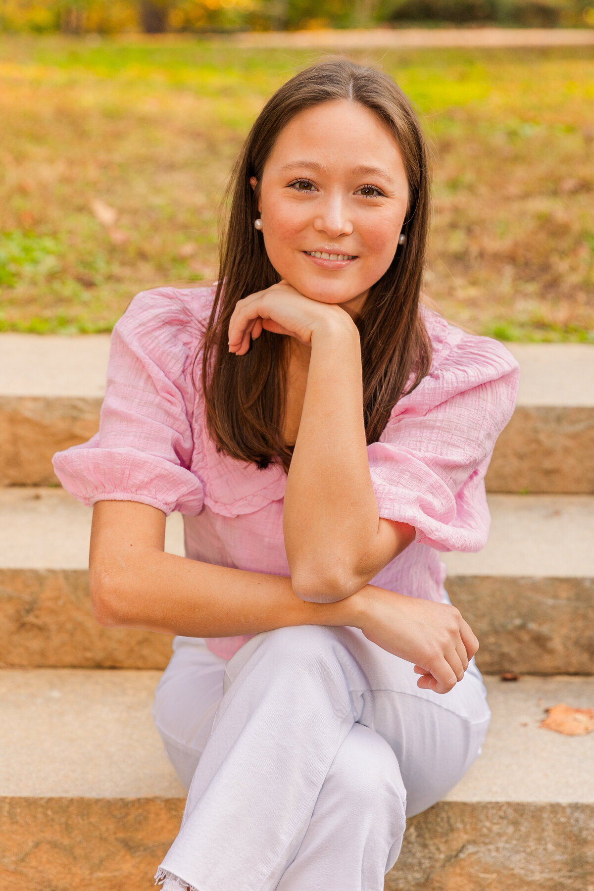 young woman sitting on a park stairs legs crossed and chin resting on the hand