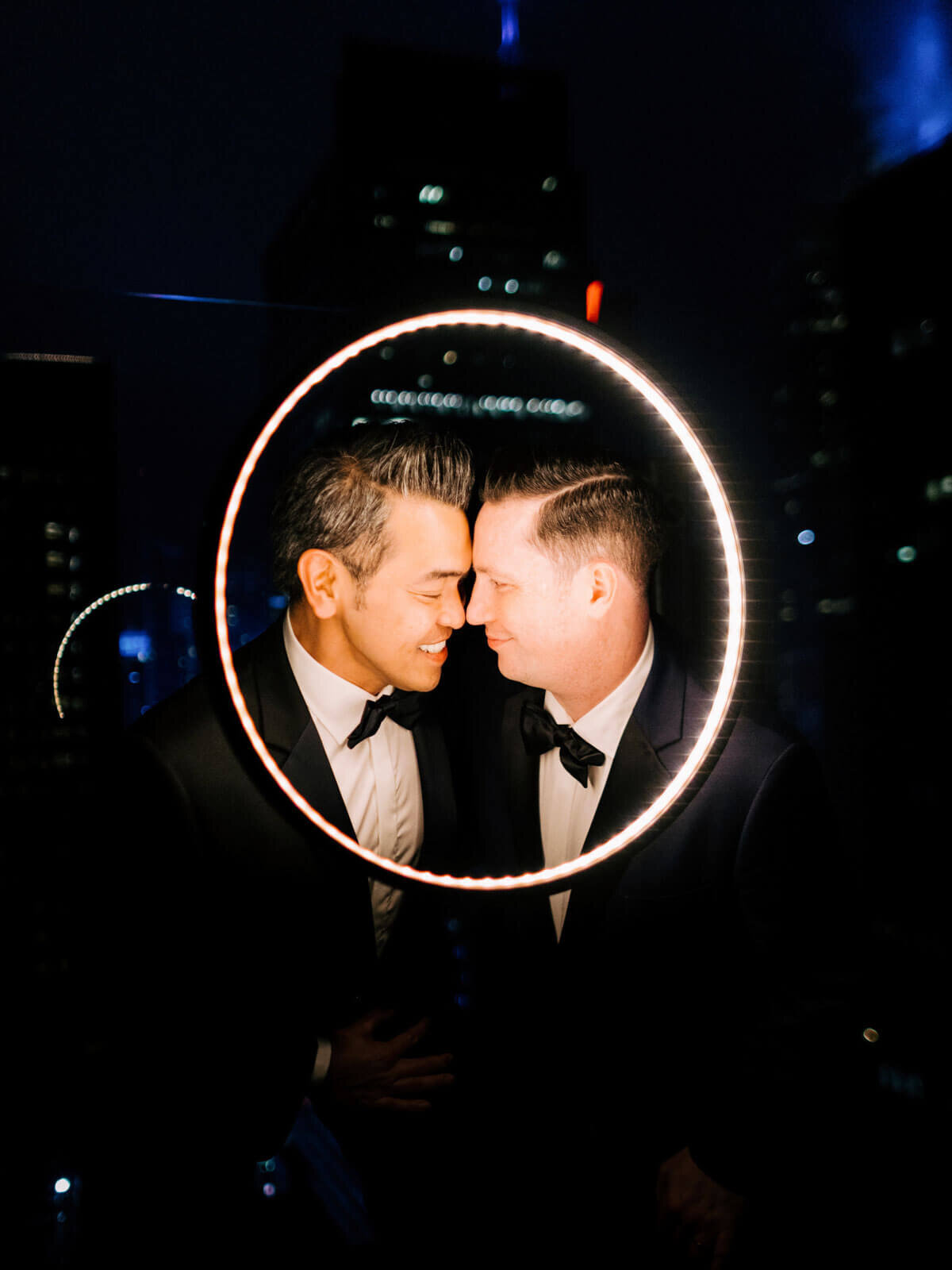 Headshot of the two grooms, heads touching, inside a ring light in The Skylark, New York. Wedding Image by Jenny Fu Studio