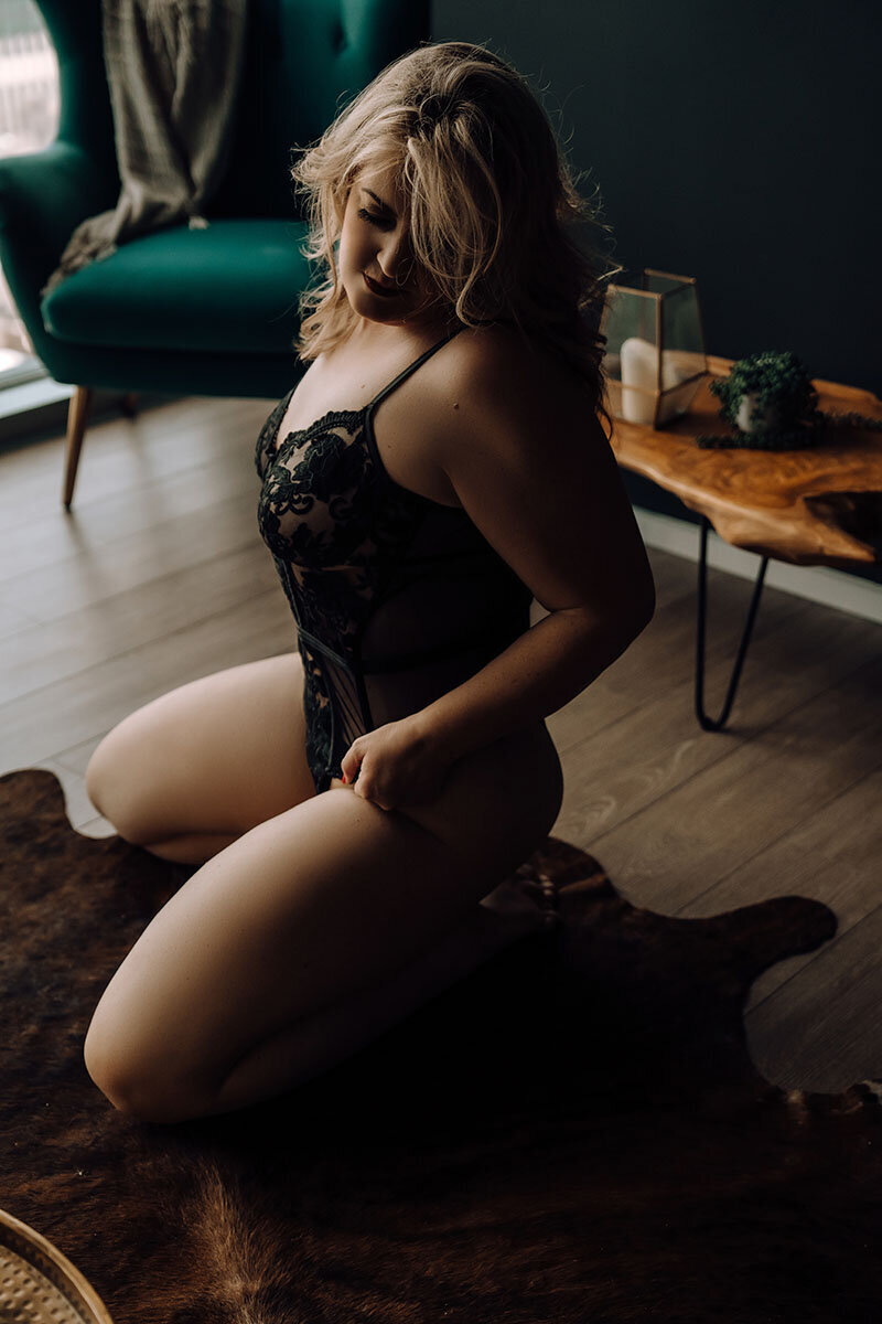 Blonde woman posing on knees in dark and moody boudoir photoshoot