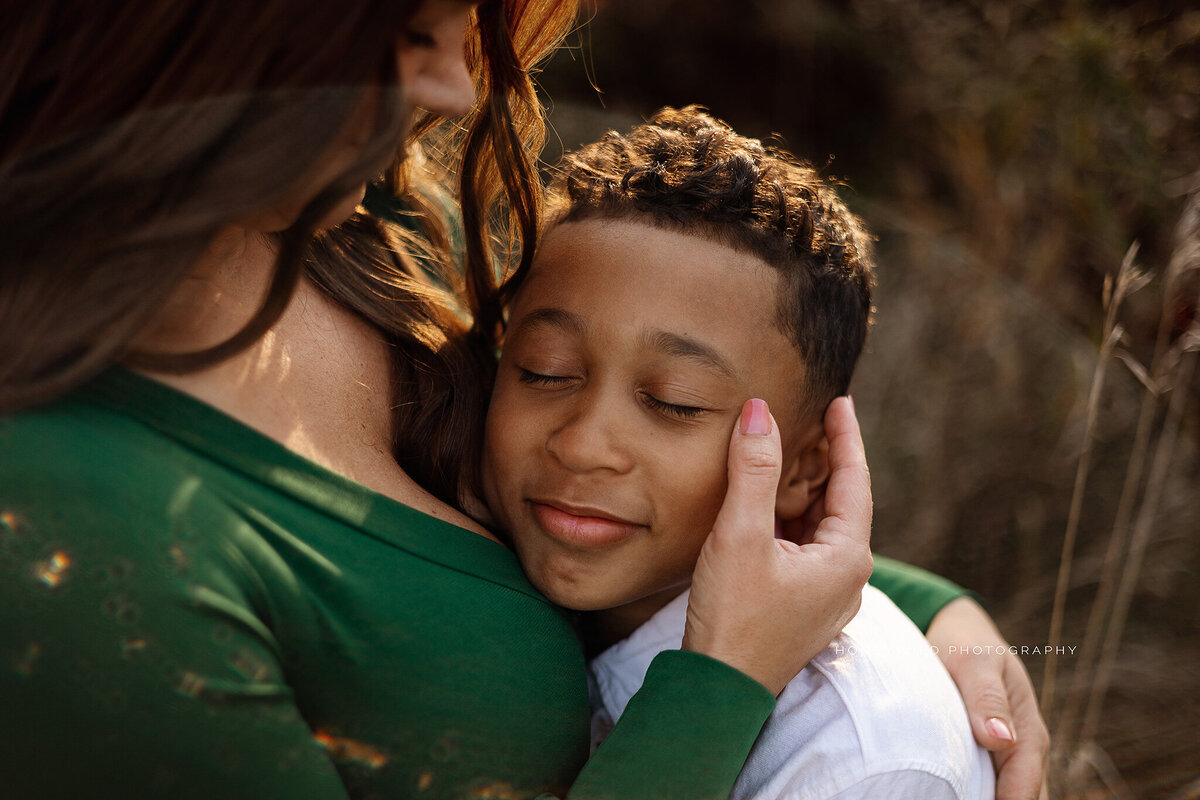 A mother gently cradles her son’s face during a family session in West Michigan, capturing the deep love and connection between parent and child.