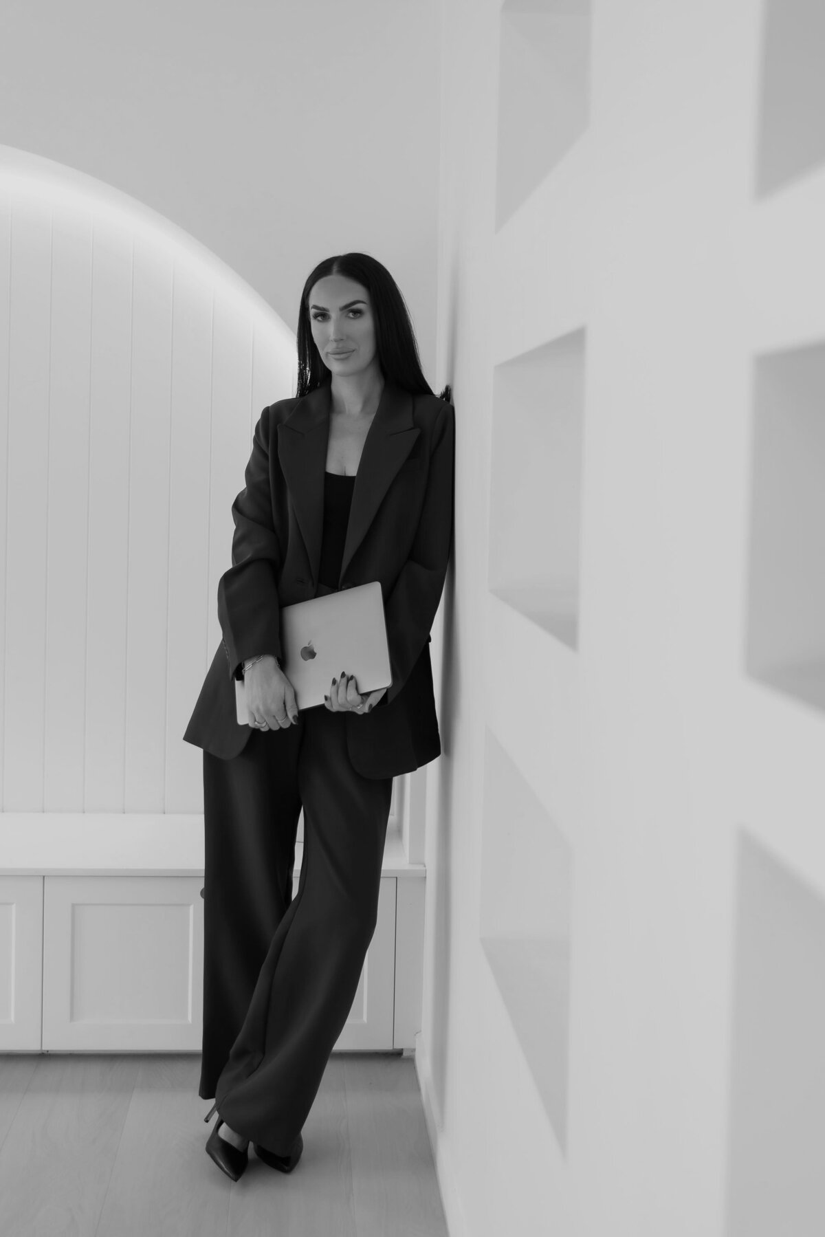 Founder Tayla Bayne holding a laptop, standing in a minimalist interior – hero image for the About page of Aurum Design Studio.