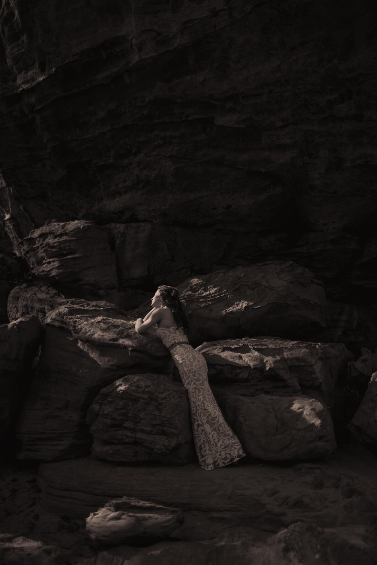 A bride leans across a boulder for her bridal portraits.