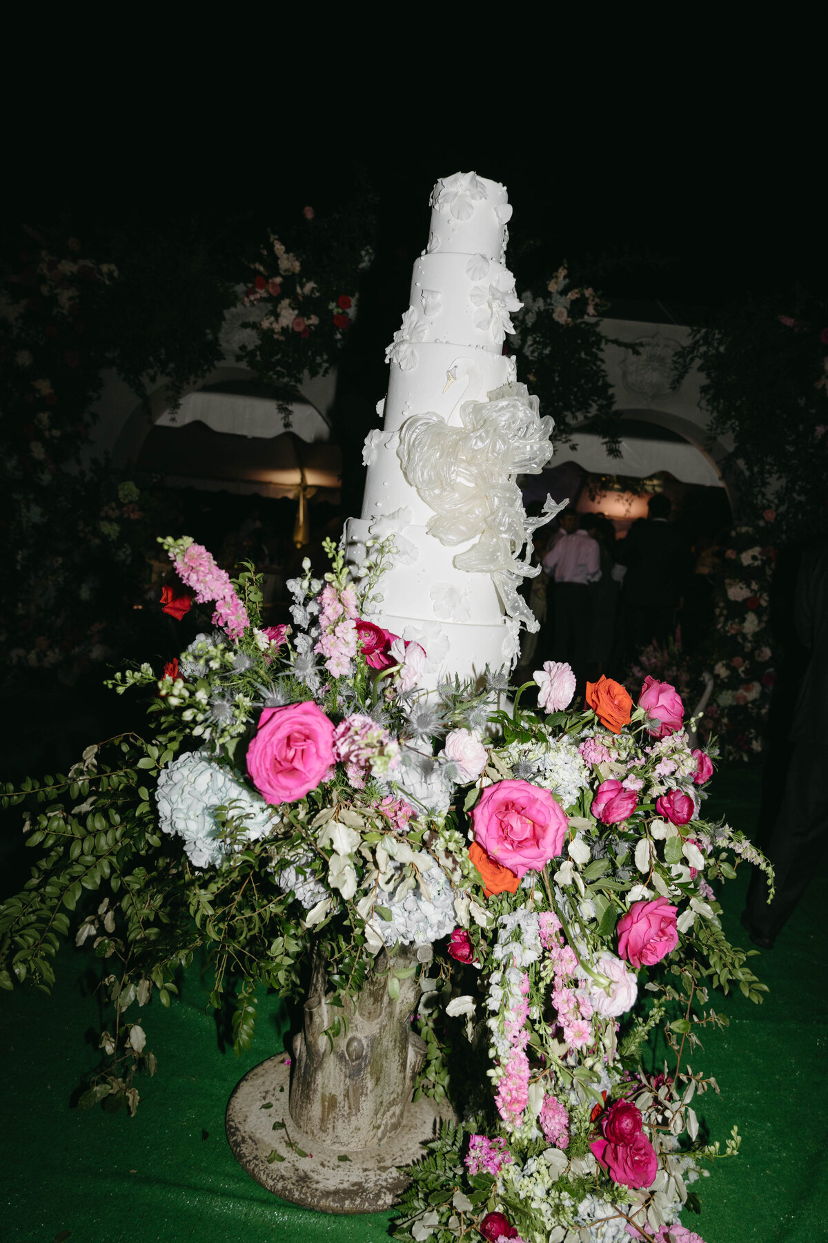 Tall white wedding cake surrounded by bright floral arrangements