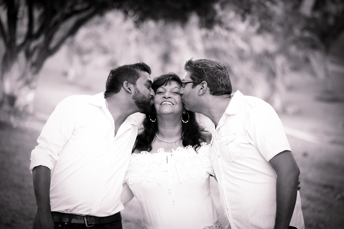 Family portrait in B+W with son and father sandwiching mom while kissing her on her cheeks. Photo by Ross Photography, Trinidad, W.I..