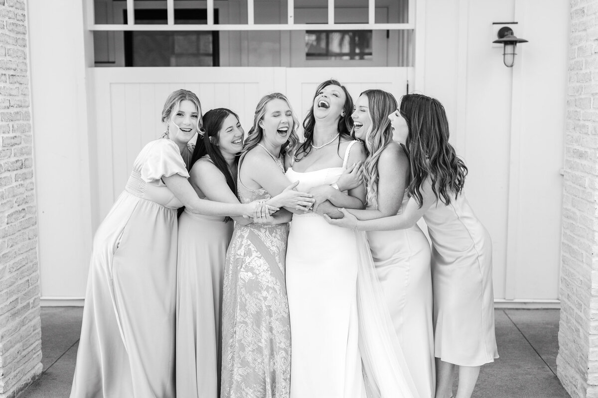 Bride and bridesmaids laughing and embracing in an elegant black and white bridal party portrait