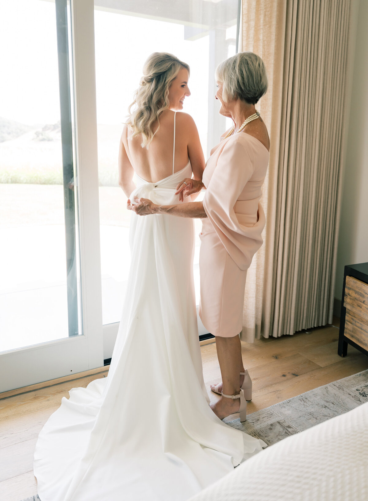 mother of bride tying bow on back of brides dress